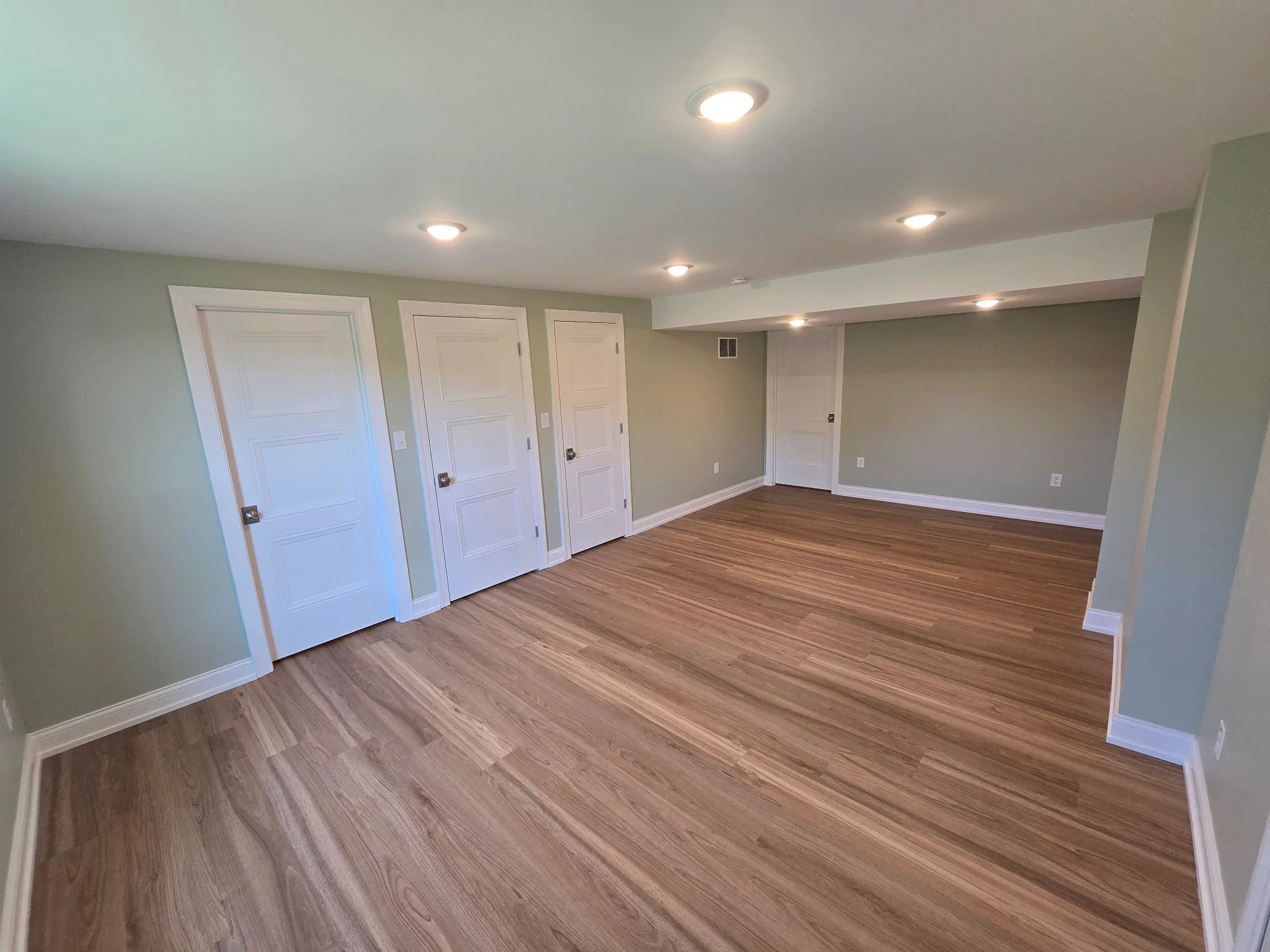Finished basement with vinyl plank flooring, recessed lighting, white doors, and neutral wall paint