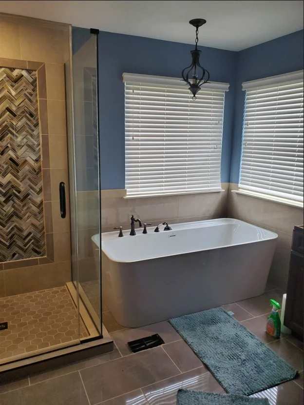 Freestanding tub, frameless shower, herringbone tile, blue walls, neutral flooring