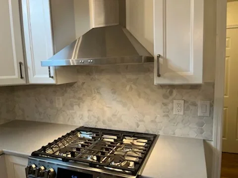 Marble subway tile backsplash with stainless steel range hood above black gas cooktop