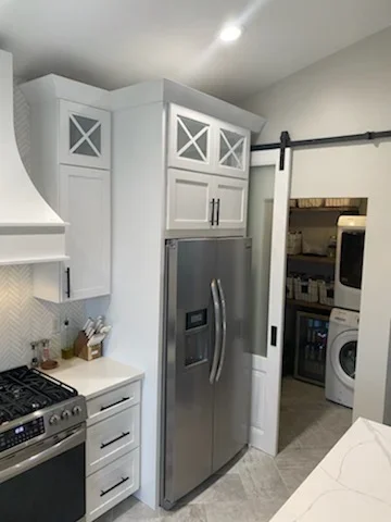 White kitchen with custom cabinetry, stainless steel appliances, subway tile backsplash, and barn door