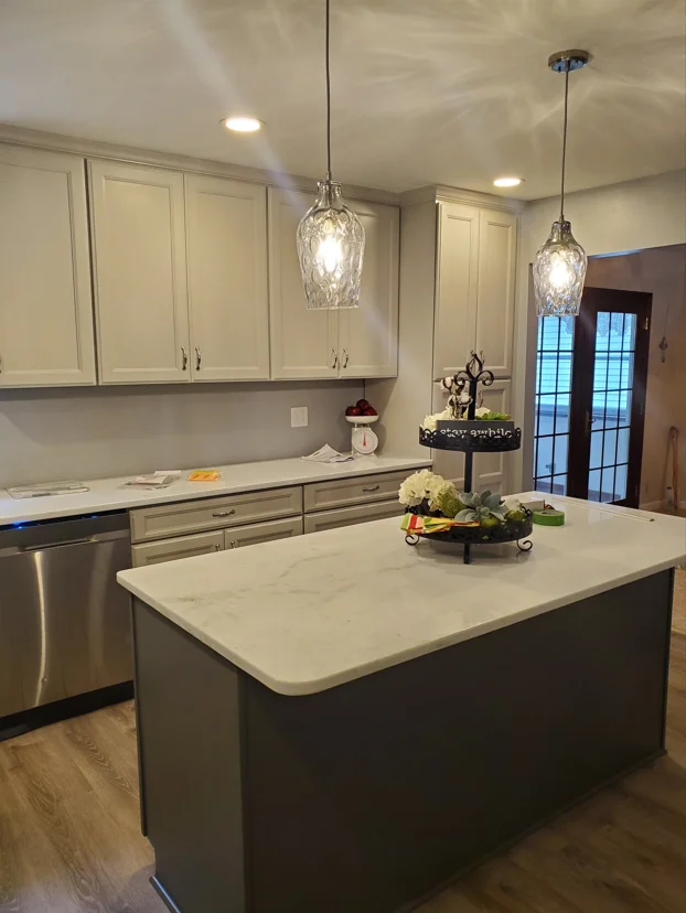 Modern kitchen with cream cabinets, dark island, white quartz counters, and glass pendant lights