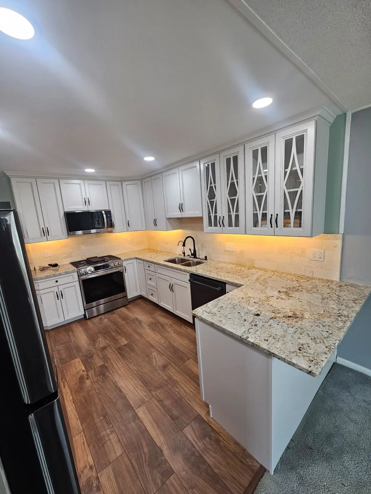 White kitchen cabinets, granite countertops, stainless steel appliances, wood flooring, LED lighting