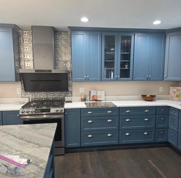 Blue shaker cabinets, marble countertops, gas range, glass-front upper cabinets, tile backsplash