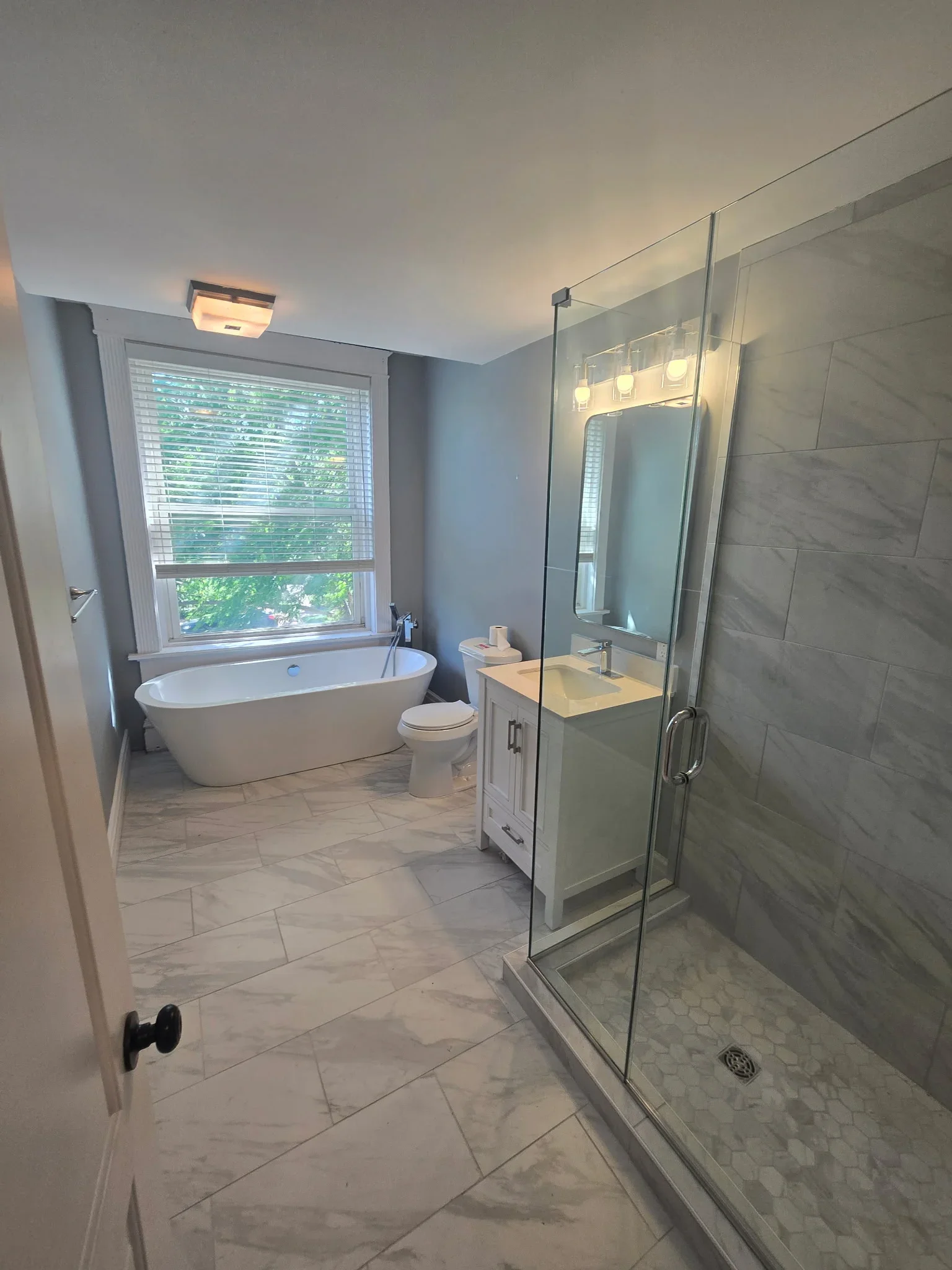 Modern bathroom with freestanding tub, frameless shower, marble tile flooring, and custom vanity