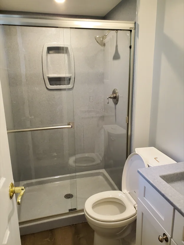 Frameless glass shower enclosure with brushed nickel frame and white ceramic fixtures in renovated bathroom