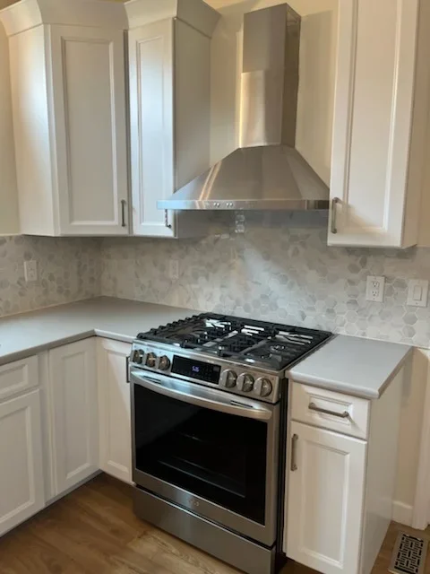 White kitchen cabinets, marble tile backsplash, stainless steel gas range and hood, quartz countertops