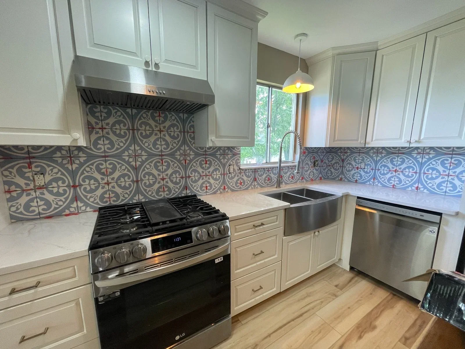 White kitchen cabinets, marble counters, geometric blue and red tile backsplash, stainless steel appliances
