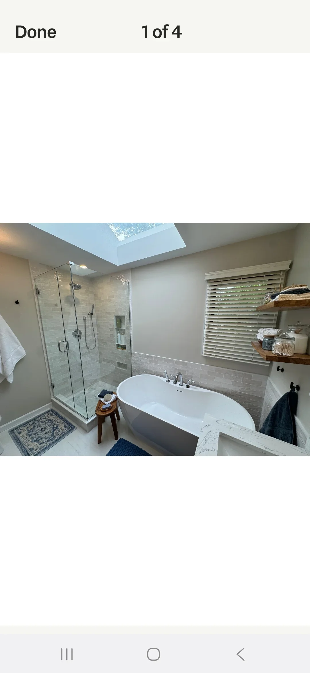 Modern bathroom with frameless shower, freestanding tub, marble counters, and skylight