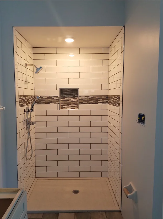 White subway tile shower with mosaic accent band, recessed shelving, and dual showerheads