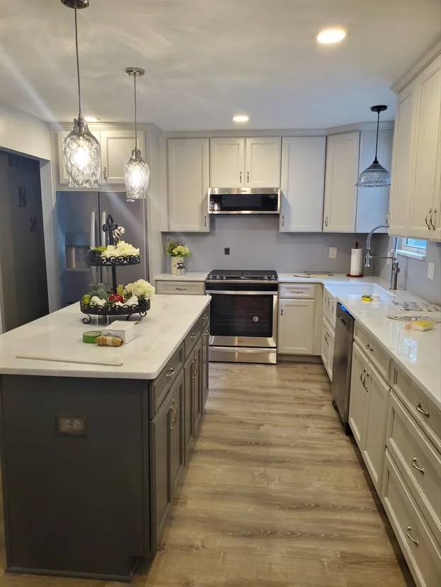 Modern kitchen with cream cabinets, dark island, white counters, stainless appliances, and pendant lights