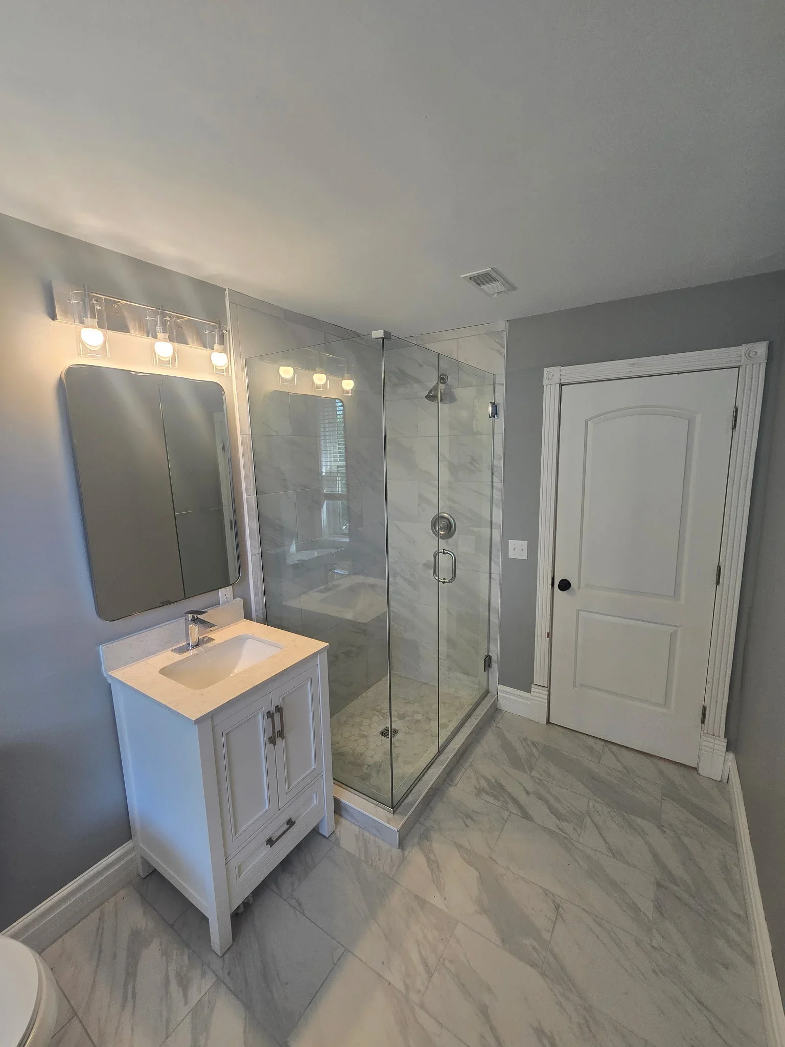 Modern bathroom with marble tile flooring, frameless glass shower, white vanity, and quartz countertop