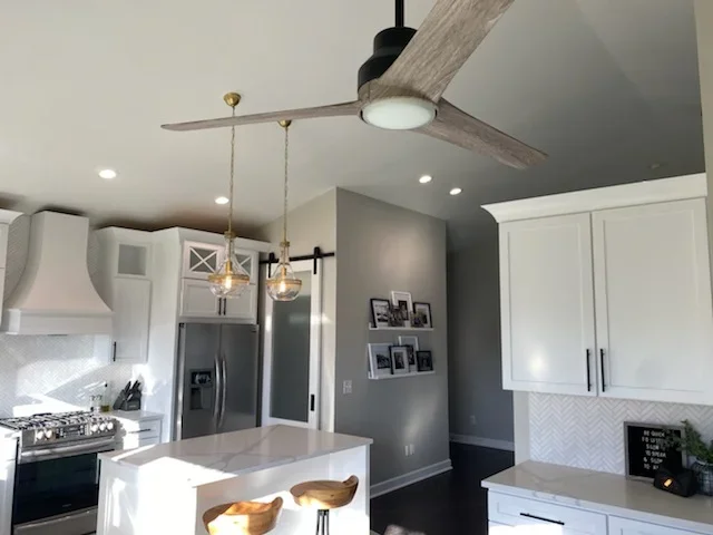 Modern kitchen with white cabinets, island, stainless appliances, gray walls, and ceiling fan