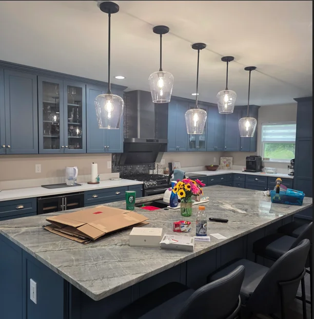 Two-tone kitchen with blue upper cabinets, black lower cabinets, marble island, and glass pendant lights
